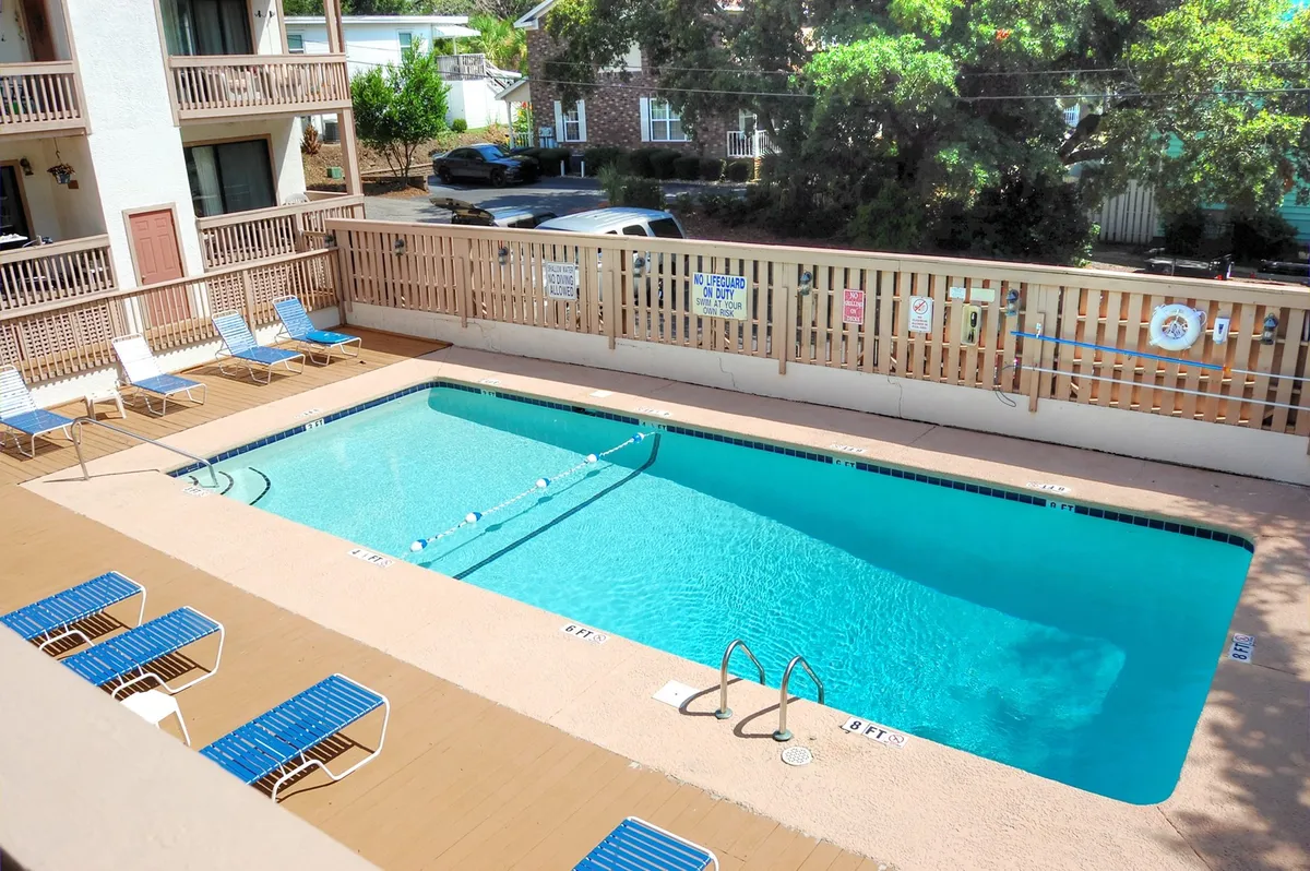 The image showcases the inviting outdoor swimming pool at Harbourside Condominiums, surrounded by comfortable lounge chairs and lush greenery, creating a tranquil yet social atmosphere perfect for relaxation and recreation. The scene is bathed in natural light, evoking a leisurely mood, and hints at activities like swimming, sunbathing, and socializing in a resort-like setting.