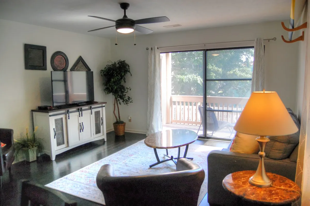 A bright and open living area featuring a plush sleeper sofa, a stylish coffee table, a wall-mounted television, and large windows that let in abundant natural light. Greenery from a potted plant further softens the space and creates a comfortable, welcoming atmosphere ideal for relaxation and socializing.